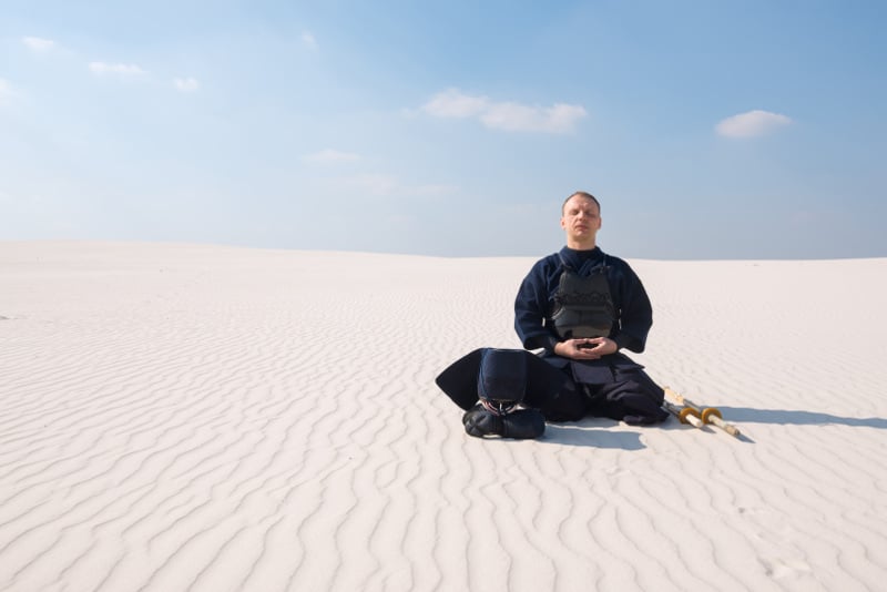 man in the desert in martial arts gear meditating