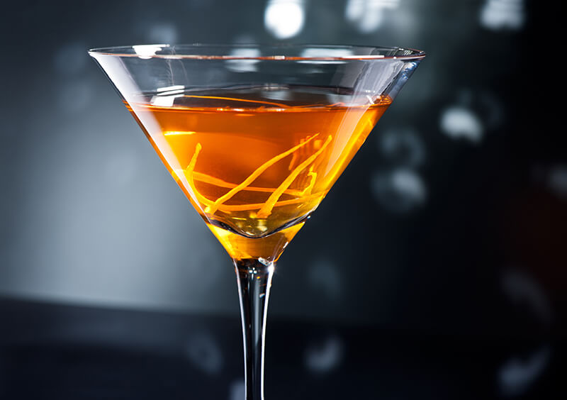 a Manhattan cocktail with orange peel against a black background
