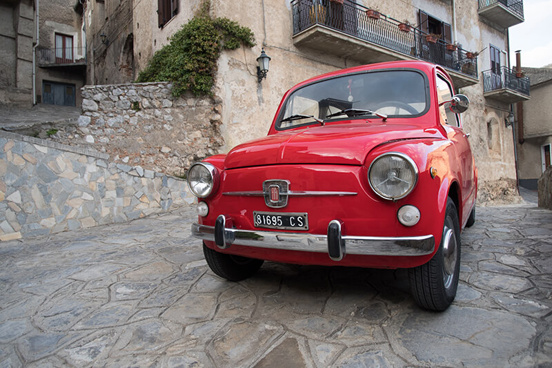 red 1965 Fiat 500 in front of a stone house in Tuscany Italy