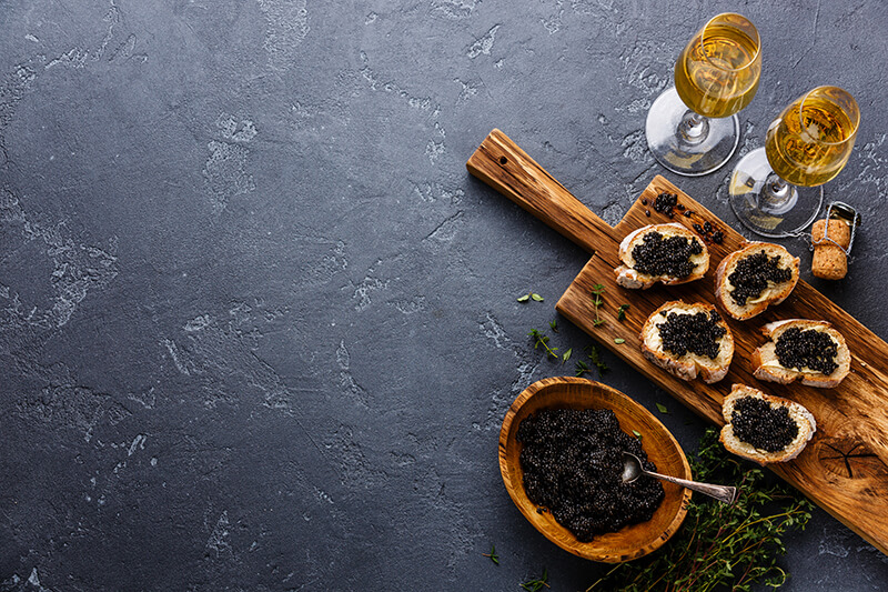 sturgeon caviar on a wooden board with white wine on a black counter 