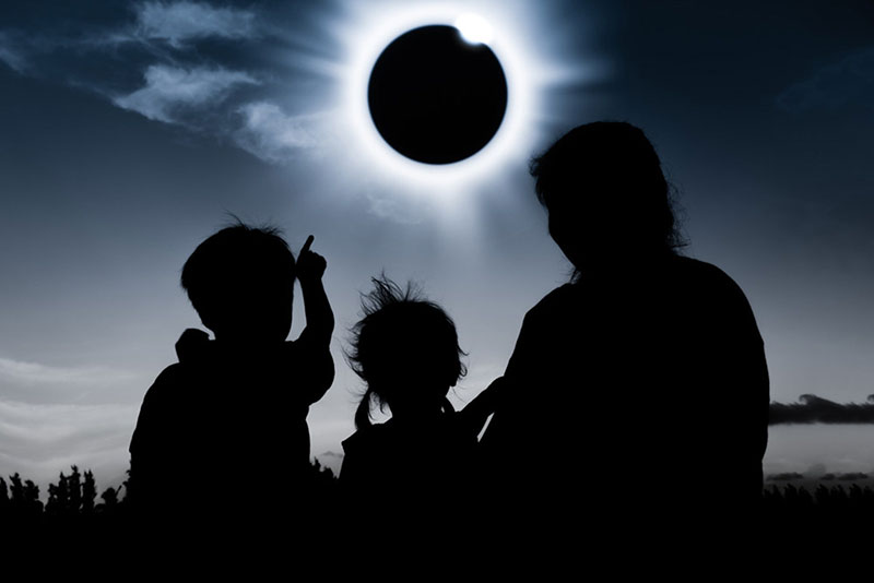 Family in silhouette gazing at a solar eclipse