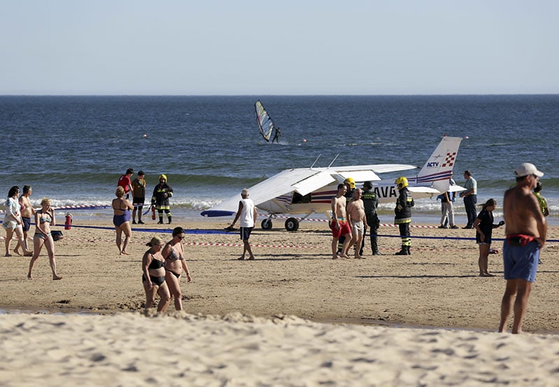 People walk past a small plane resting by the sea after an emergency landing at Sao Joao beach in Costa da Caparica outside 