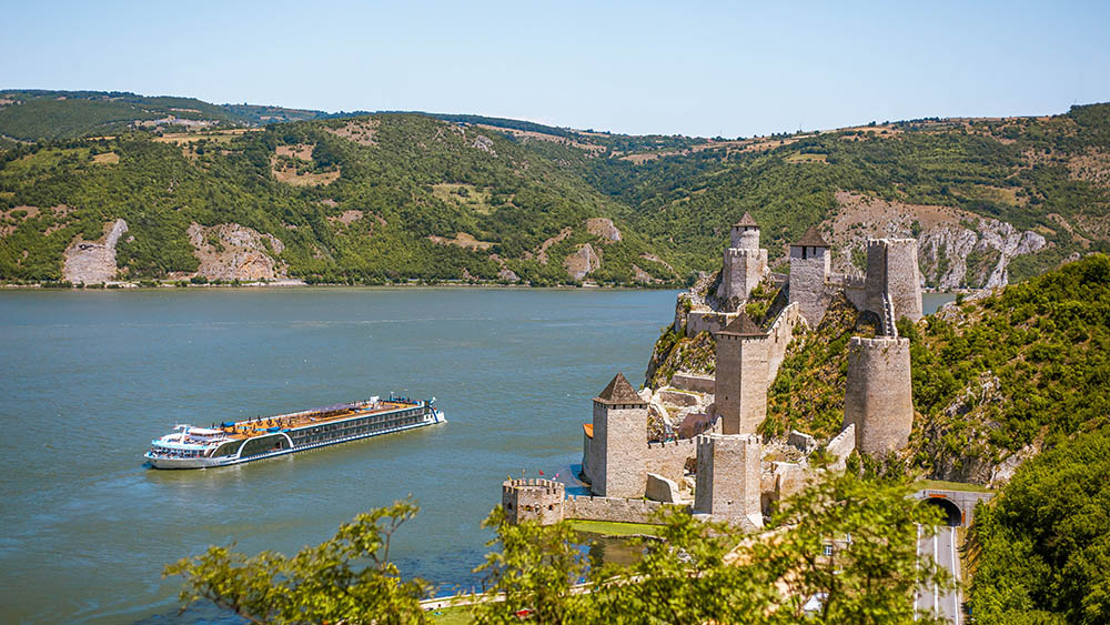 A river cruise vessel with a castle on the shore