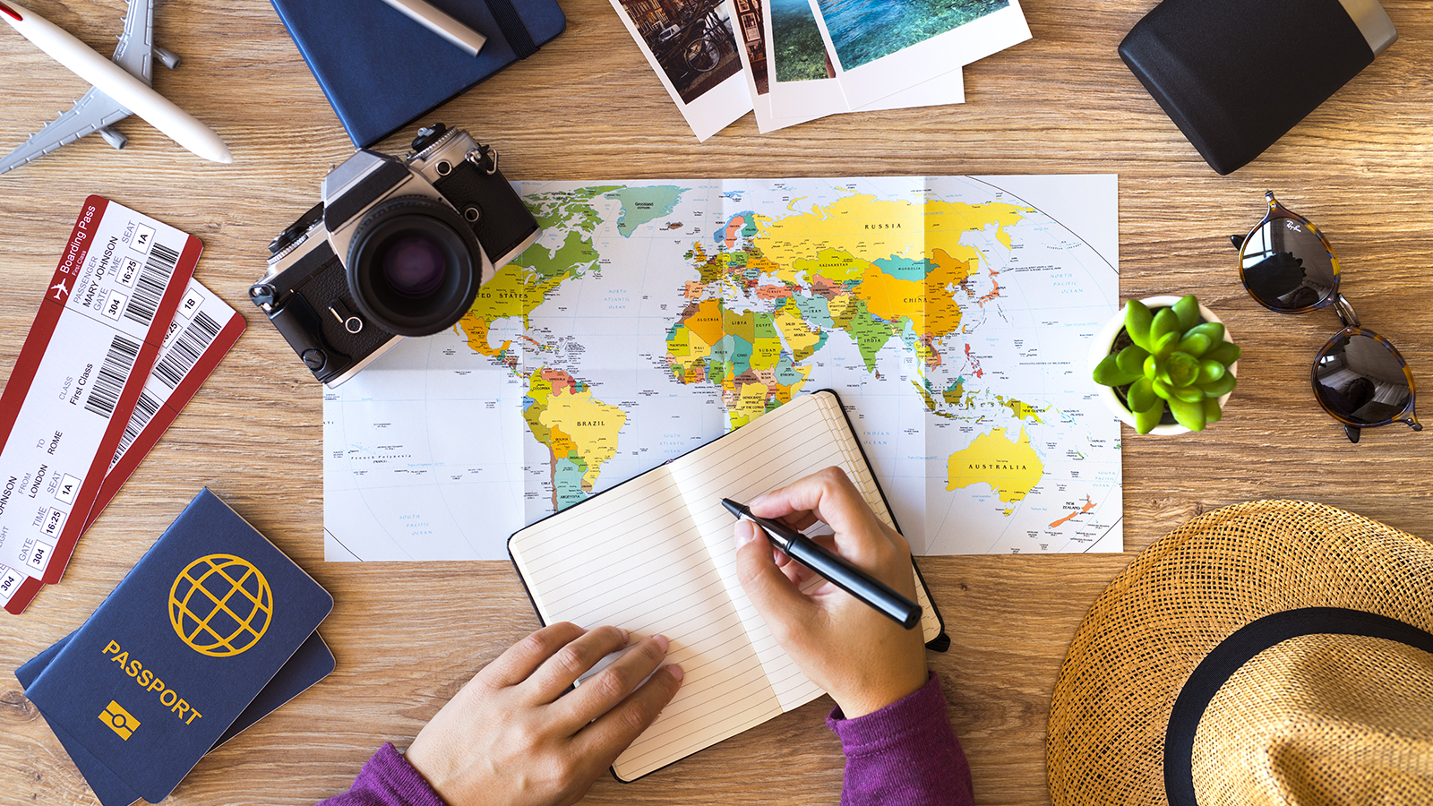 woman writing in book surrounded by map camera passport and plane tickets