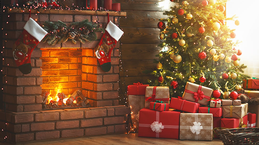 Christmas tree with gifts underneath next to a fireplace with stockings