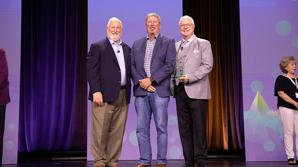 Three men standing on a stage with an award