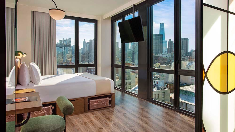 A hotel guestroom with floor to ceiling windows and views of the World Trade Center