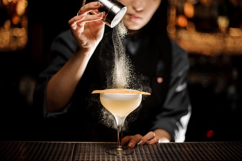 A bartender sprinkles sugar over her cocktail 