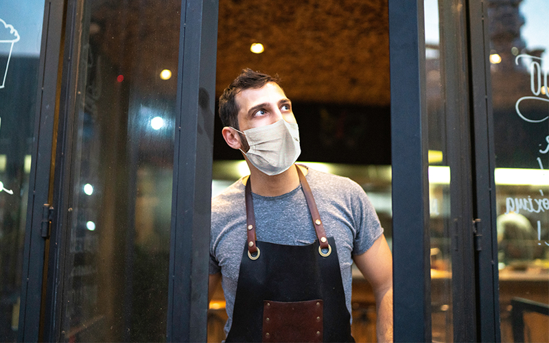 A restaurant owner looks out the door of his COVID-era restaurant wearing a mask