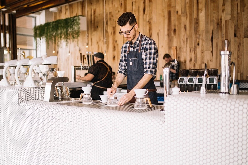 A barista stands at the counter of a white-tiled coffee shop