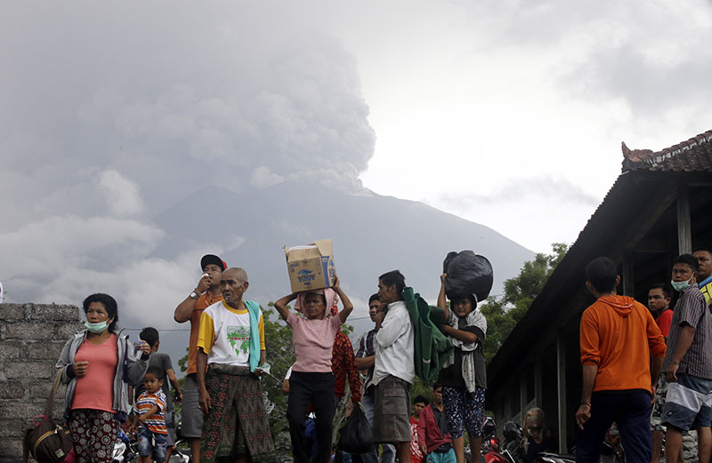 Villagers carry their belongings during an evacuation following the eruption of Mount Agung seen in the background in Karan