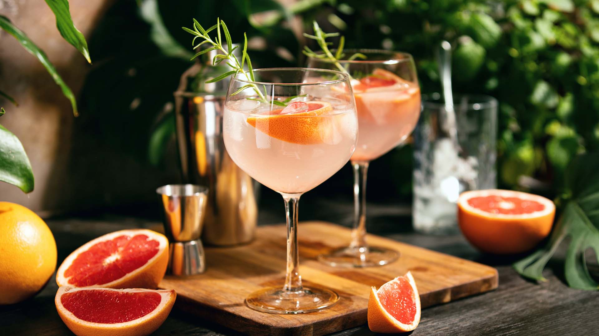 A beautiful pink cocktail is served in a coupe glass with a rosemary garnish