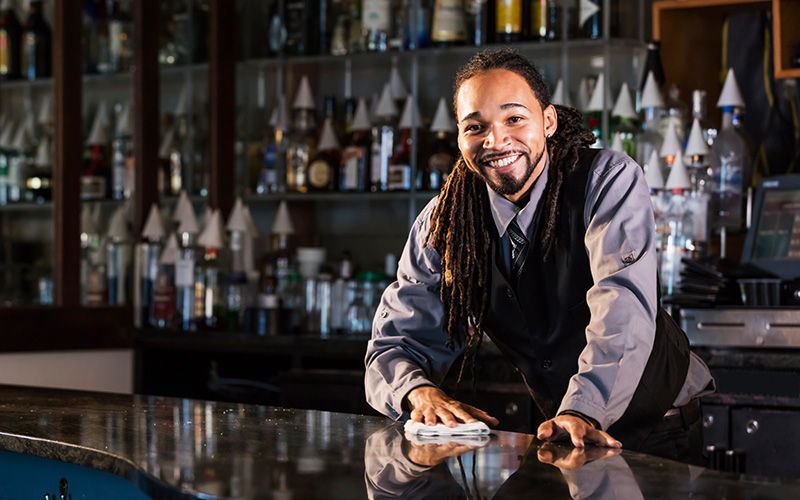 A young bartender poses with a smile from behind his bar