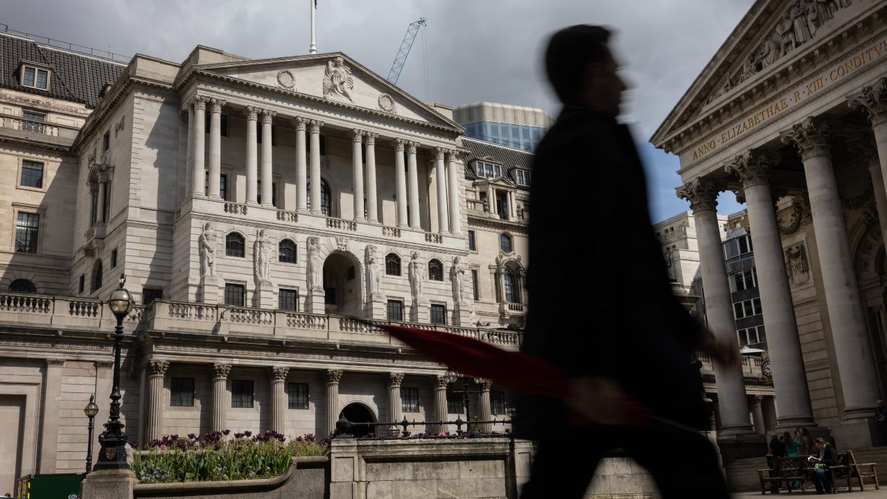 A man holding an umbrella walks past the Bank of England