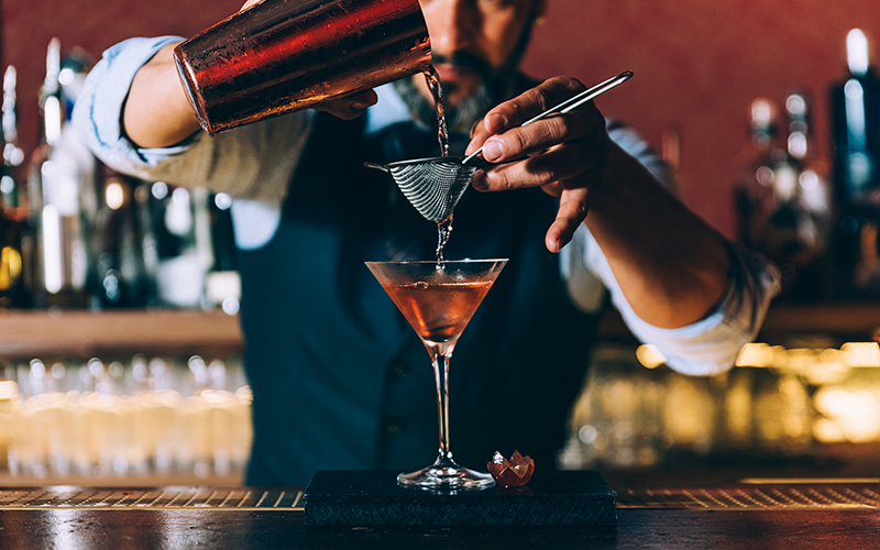 A bartender pours a drink into a martini glass