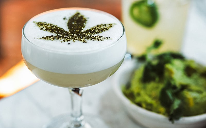 a cannabis infused cocktail with a cannabis leaf stenciled on top 
