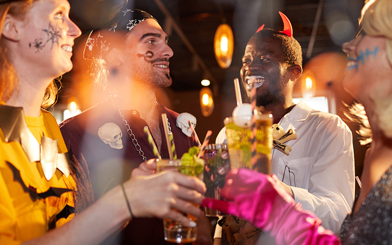 friends wearing Halloween costumes drinking cocktails while enjoying party in club and having fun