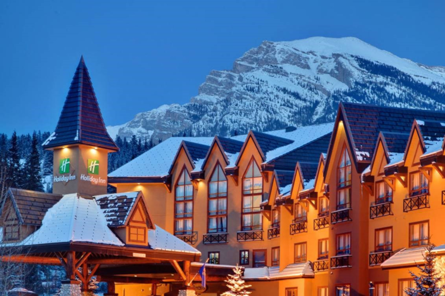 The exterior of the Holiday Inn Canmore with a snowy mountain behind it