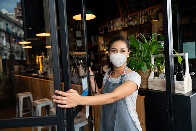 Woman wearing mask opening door to restaurant
