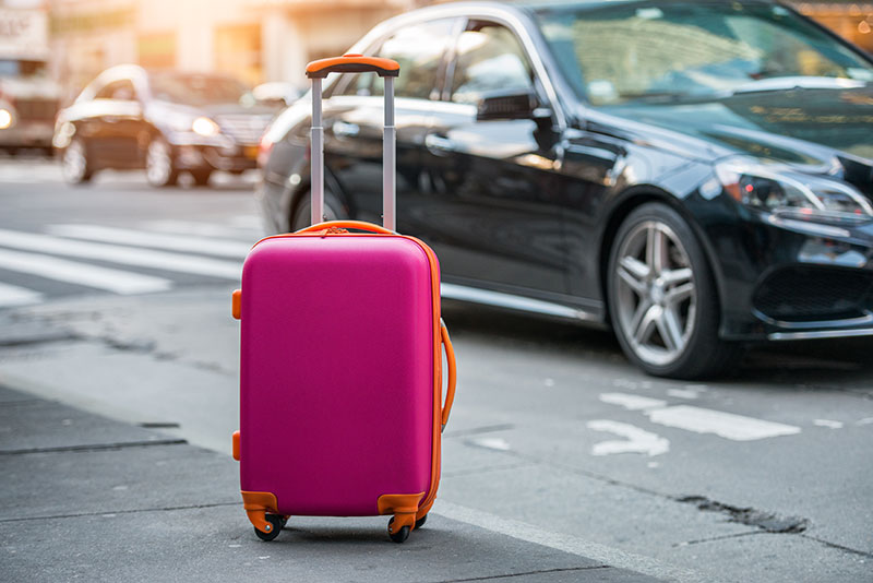 Luggage bag on the city street ready to pick by airport transfer taxi car