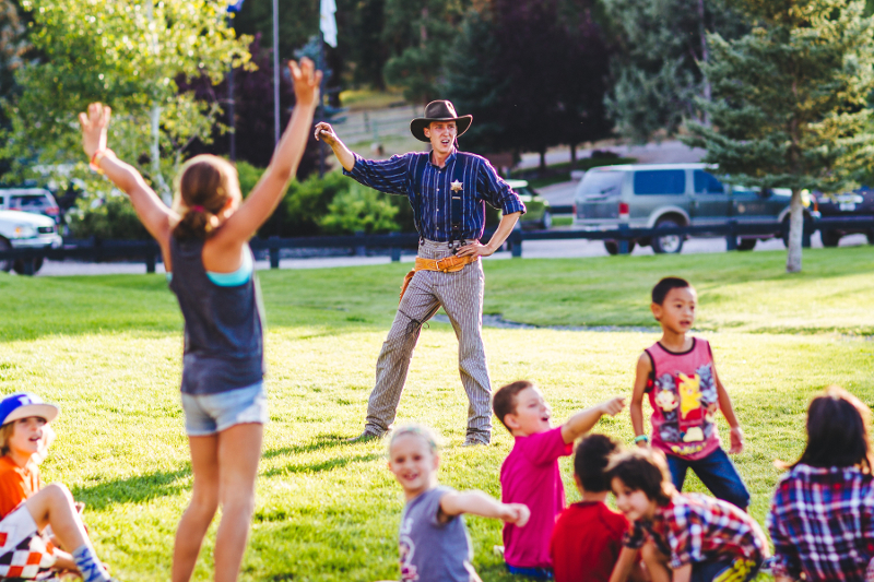 Kids stand around with a man in a cowboy hat in the background