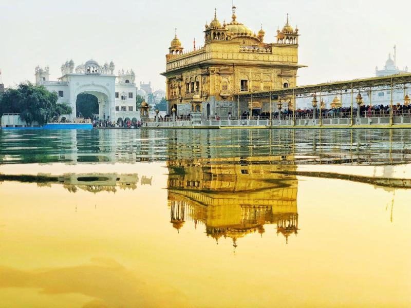 The Golden Temple is reflected in the wet pavement