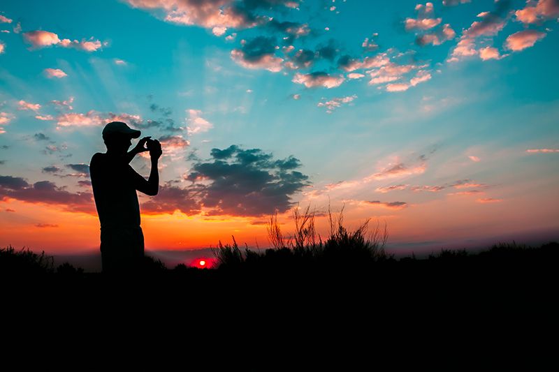 man taking photo with smartphone at sunrise