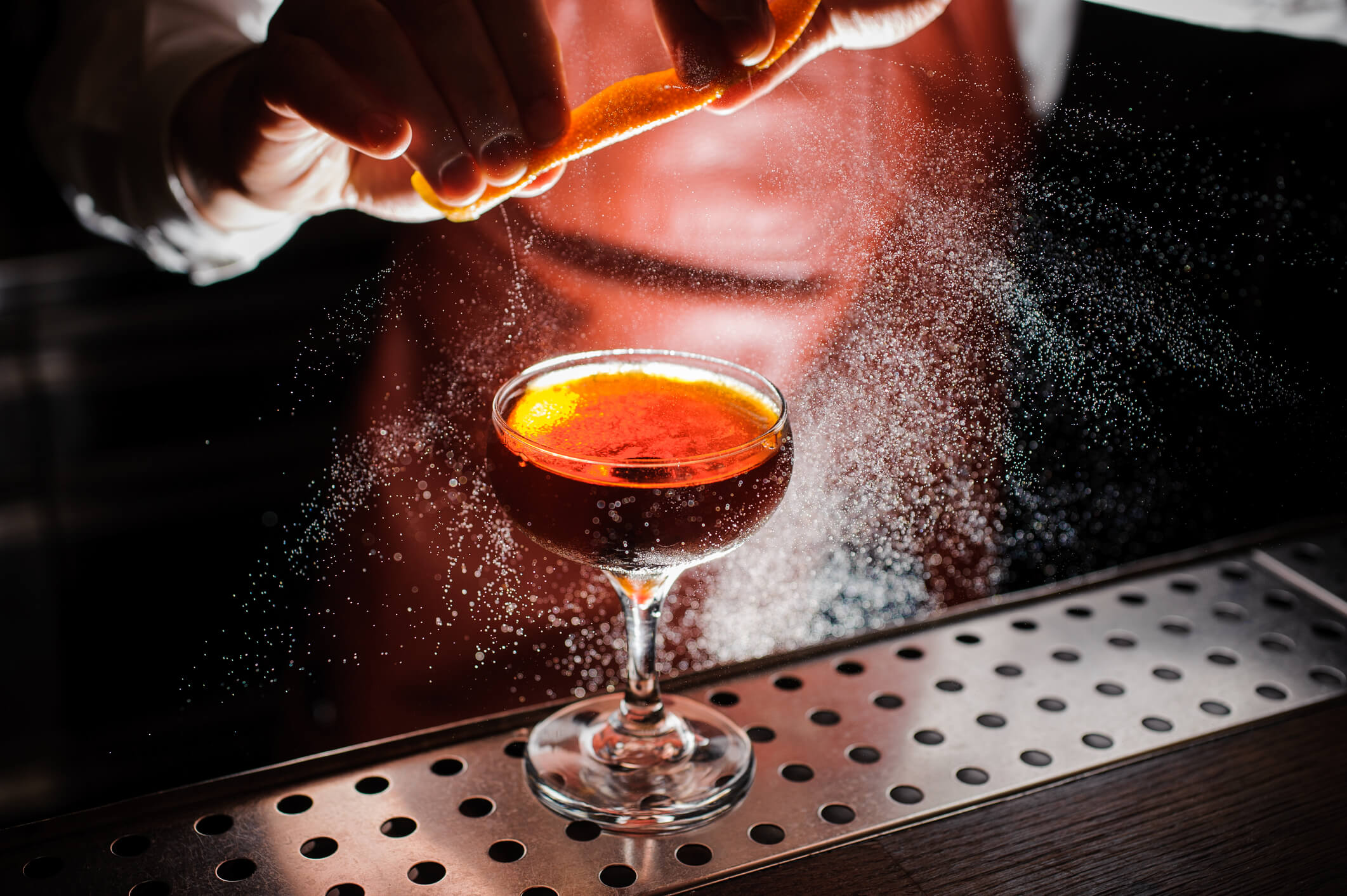 Bartender expressing orange slice over cocktail