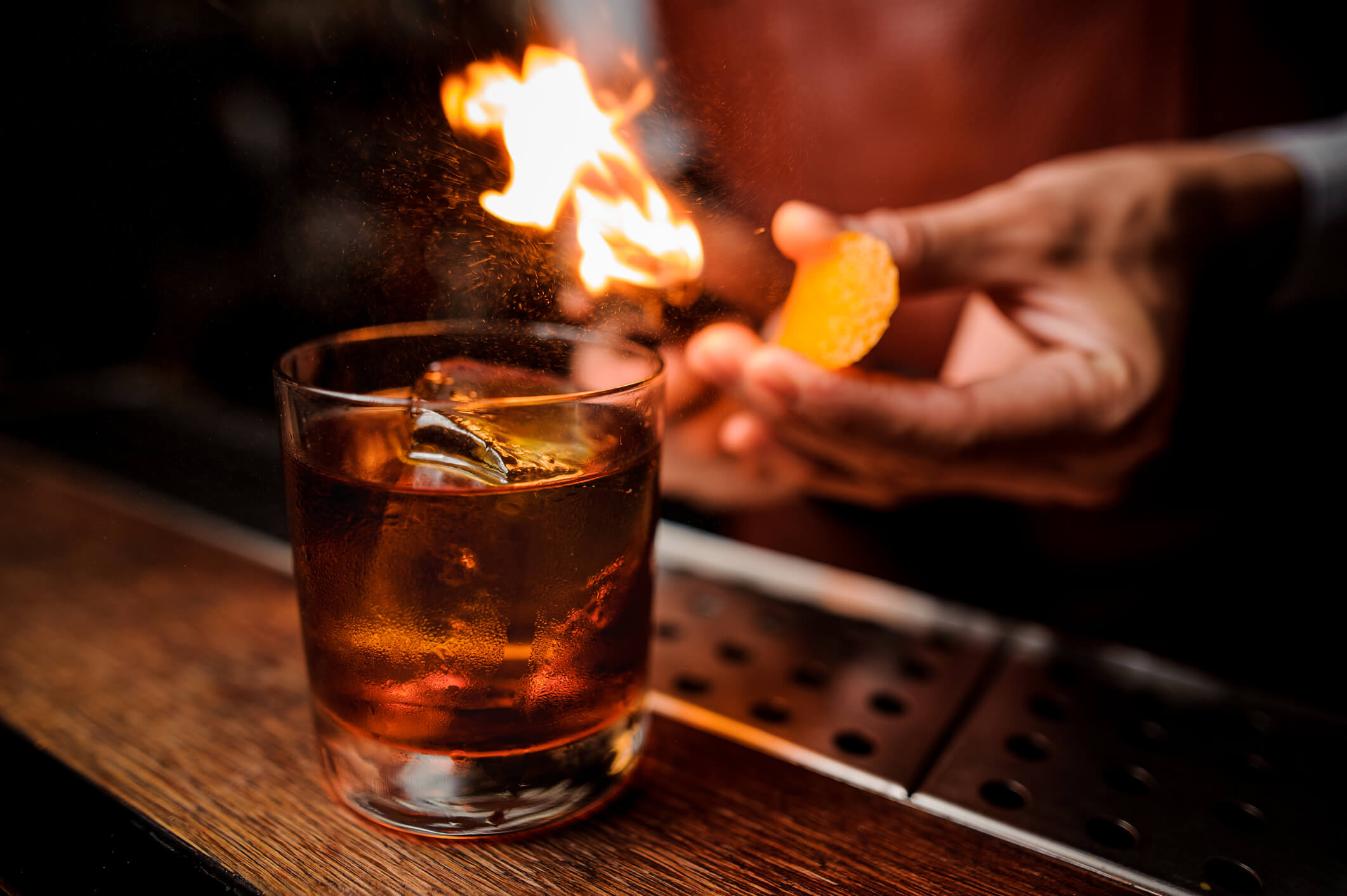 Bartender flaming an orange peel over a cocktail