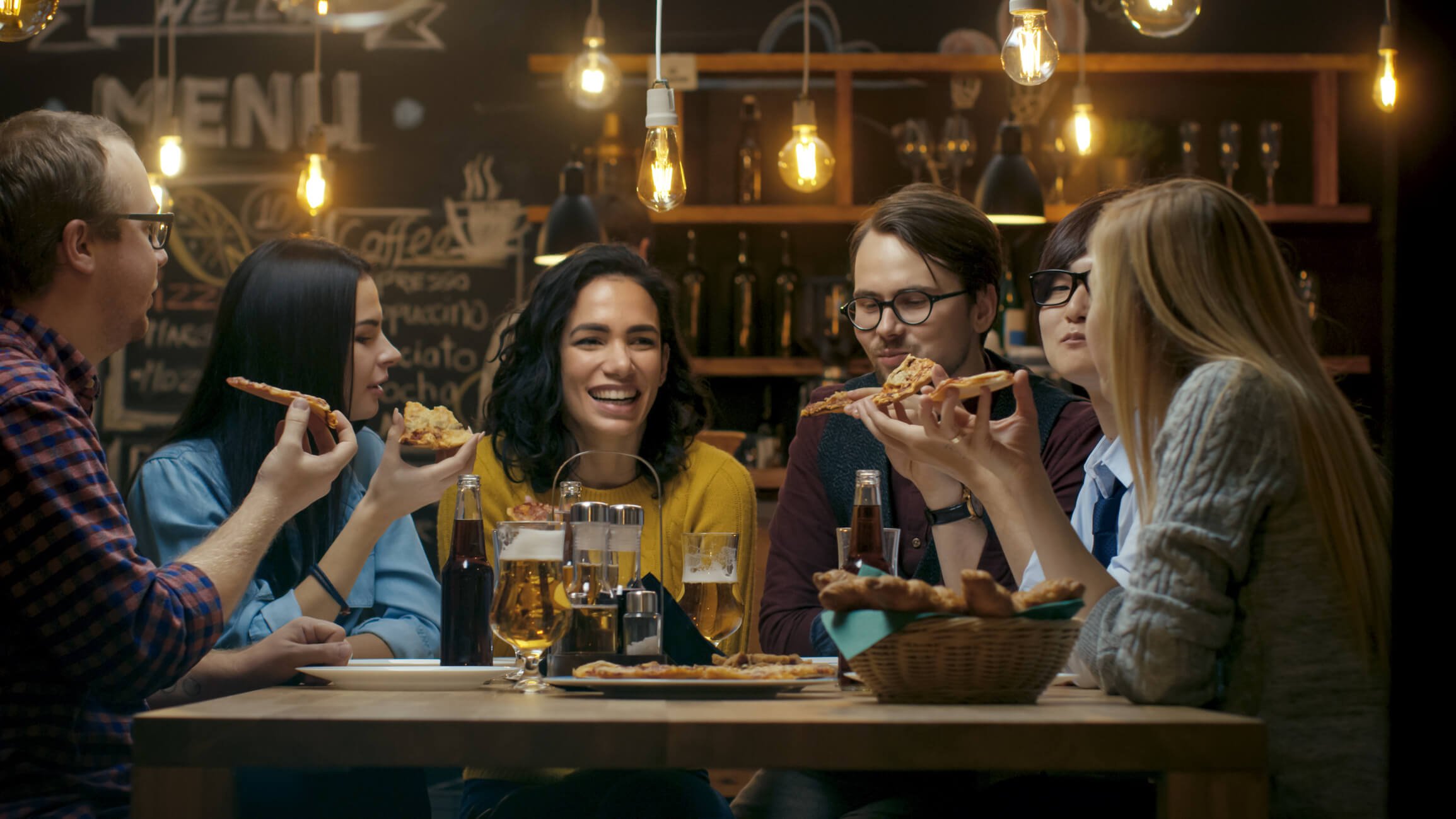 Group of happy diverse young people eat pizza at a restaurant