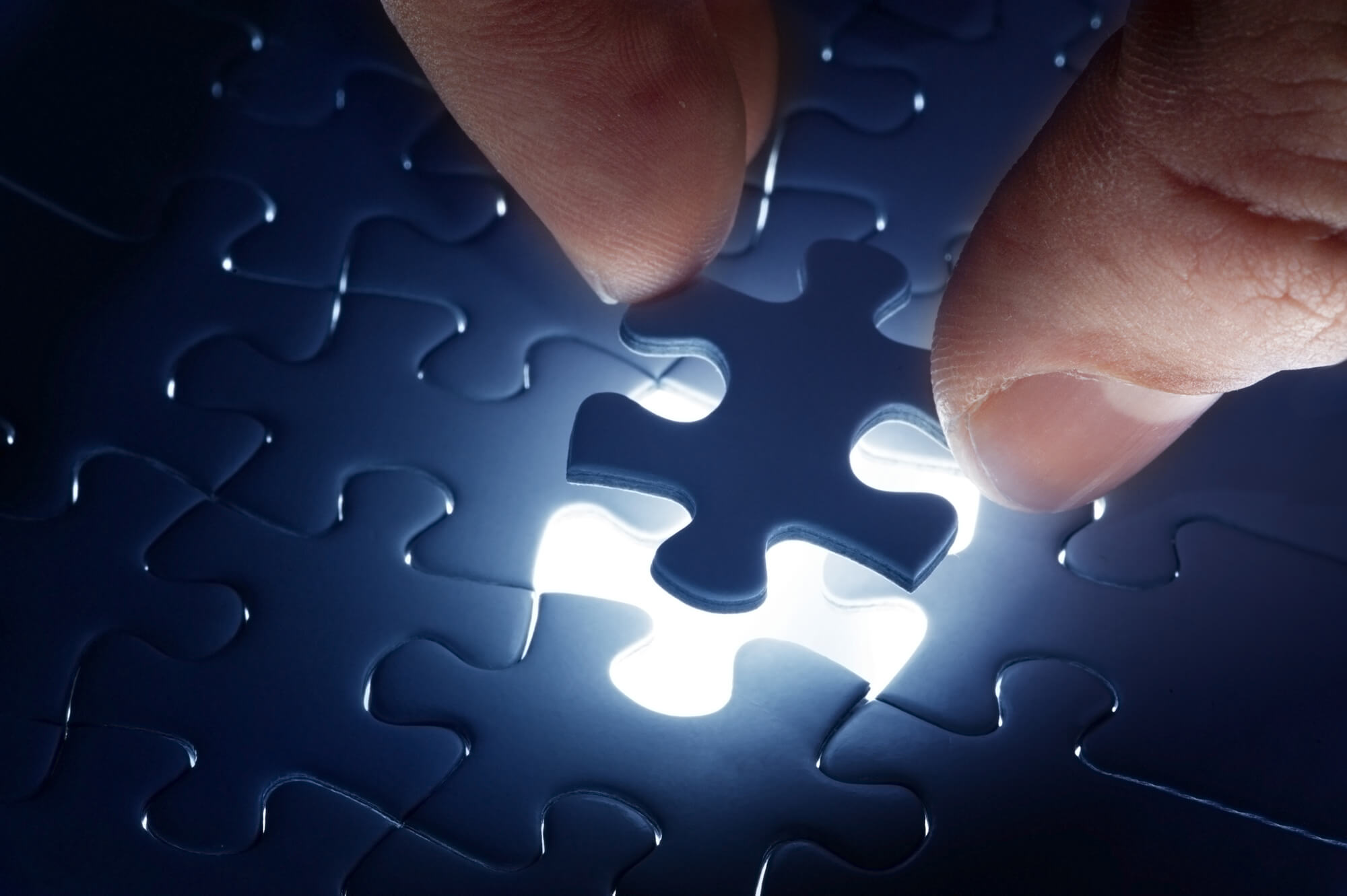 Hand adding final glowing puzzle piece for business concept