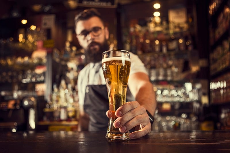 A bartender holds a pint of beer on a bar