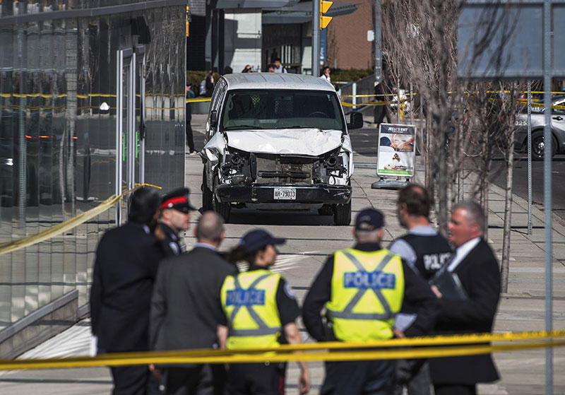 Police are seen near a damaged van after a van mounted a sidewalk crashing into pedestrians in Toronto 