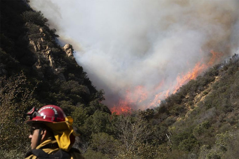 A firefighter monitors a wildfire burning along a hillside in Malibu CA