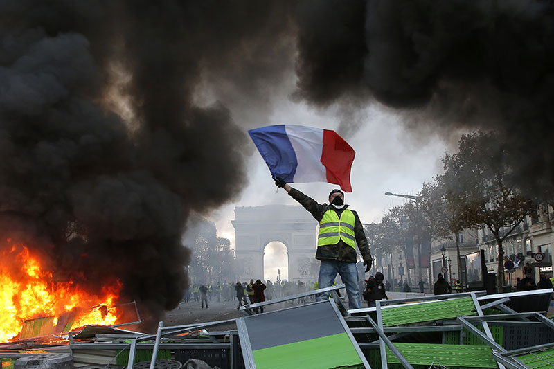 A demonstrator waves the French flag on a burning barricade on the Champs-Elysees avenue with the Arc de Triomphe in backgrou