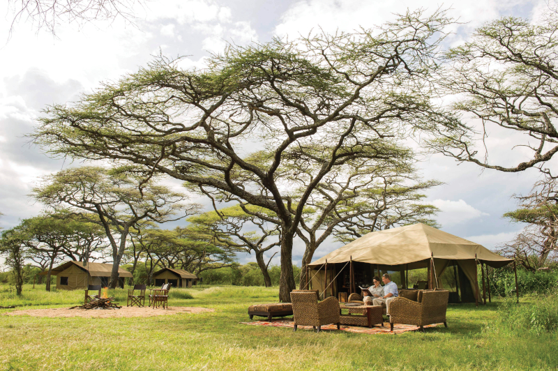 Two people sit outside a tent at the Legendary Serengeti Mobile Camp