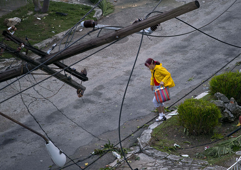 A woman walks under a lamp post toppled by a tornado in Havana Cuba