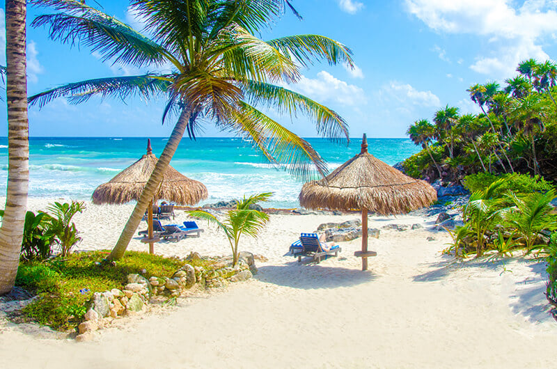 Tulum beach with thatch umbrellas and lounge chairs