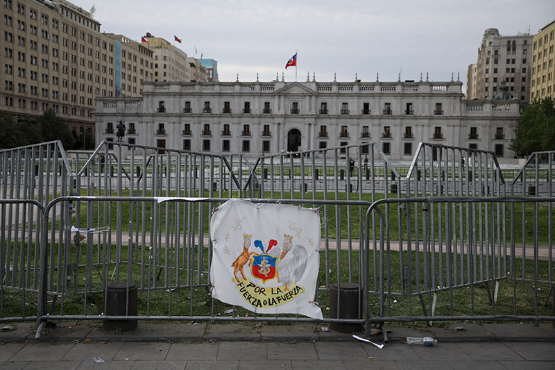 A police barricade with a fake national coat of arms that reads By force or force bars the way to La Moneda presidential p