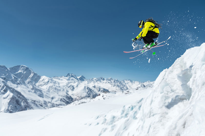 A skier in full sports equipment jumps into the precipice from the top of the glacier against the background of the blue sky 