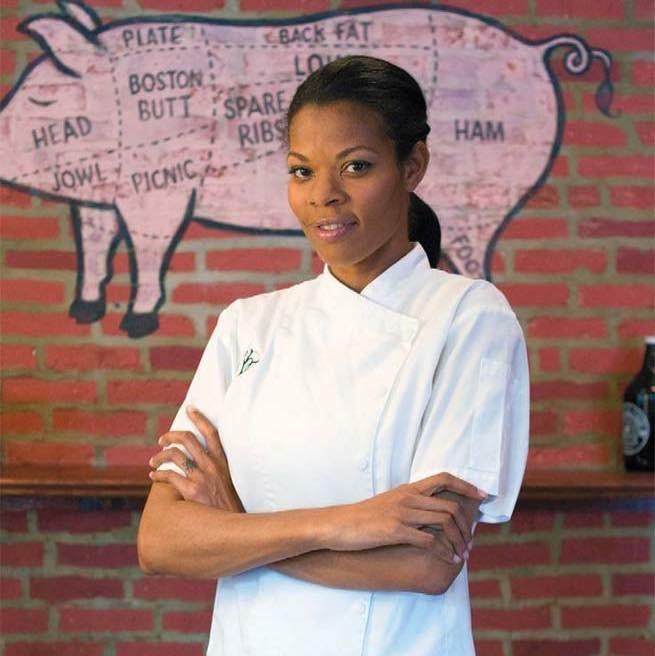 Chef Barbie Marshall poses with her arms crossed, looking at the camera. She's wearing her hair pulled back, and a white chef's coat.