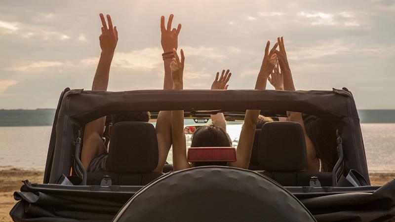 People raising arms through Jeep on a beach