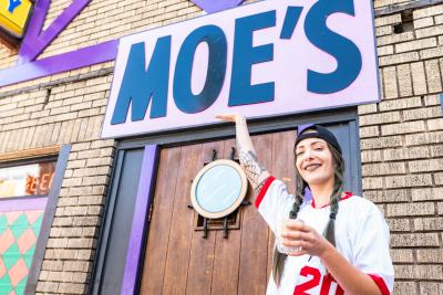 A woman in costume smiles beneath the Moe's Tavern sign