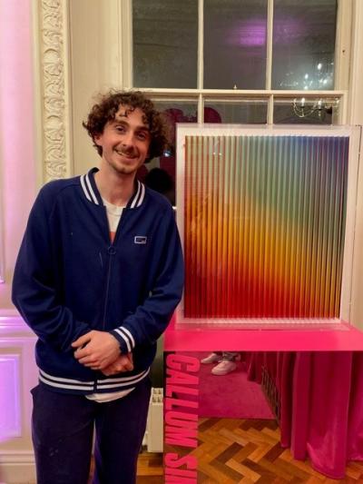 An artist in a track jacket standing next to a kinetic art piece