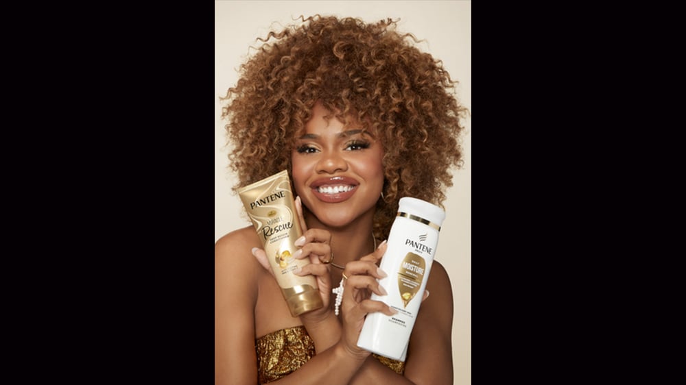 Image of beautiful black woman with curly hair holding Pantene products
