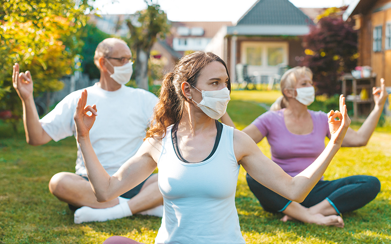 Three people in a mask doing yoga outside