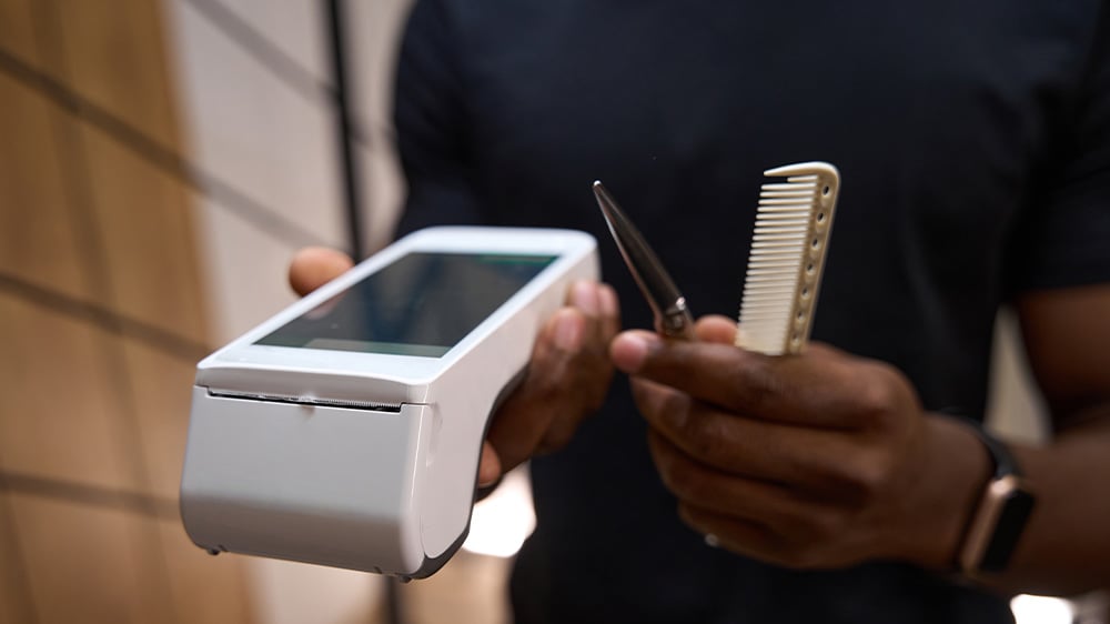 Barber holding credit card reader with scissors and comb
