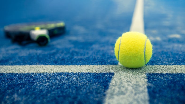 Yellow ball on floor behind paddle net in blue court outdoors