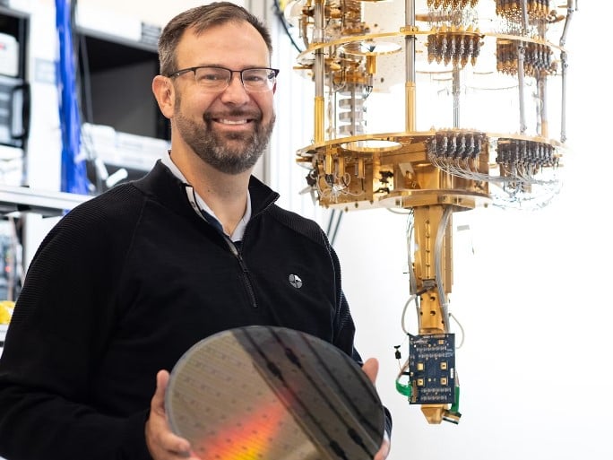Clarke holding wafer standing in front of quantum computer