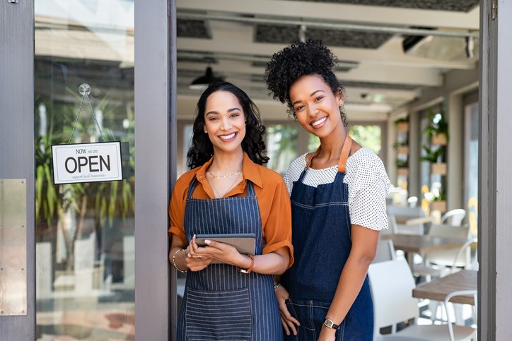 Two small business owners standing together at cafe entrance while smiling -stock images RidofranzGetty Images